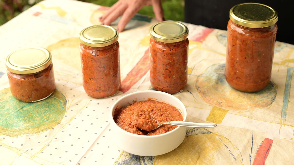 Eine Schale mit rotem Ajvar-Paprikamus, dahinter gefüllte Einmachgläser