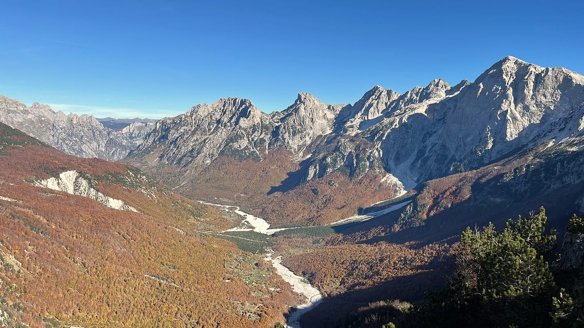 Herbstliches Bergtal in den albanischen Alpen mit schroffen Gipfeln und einem Fluss