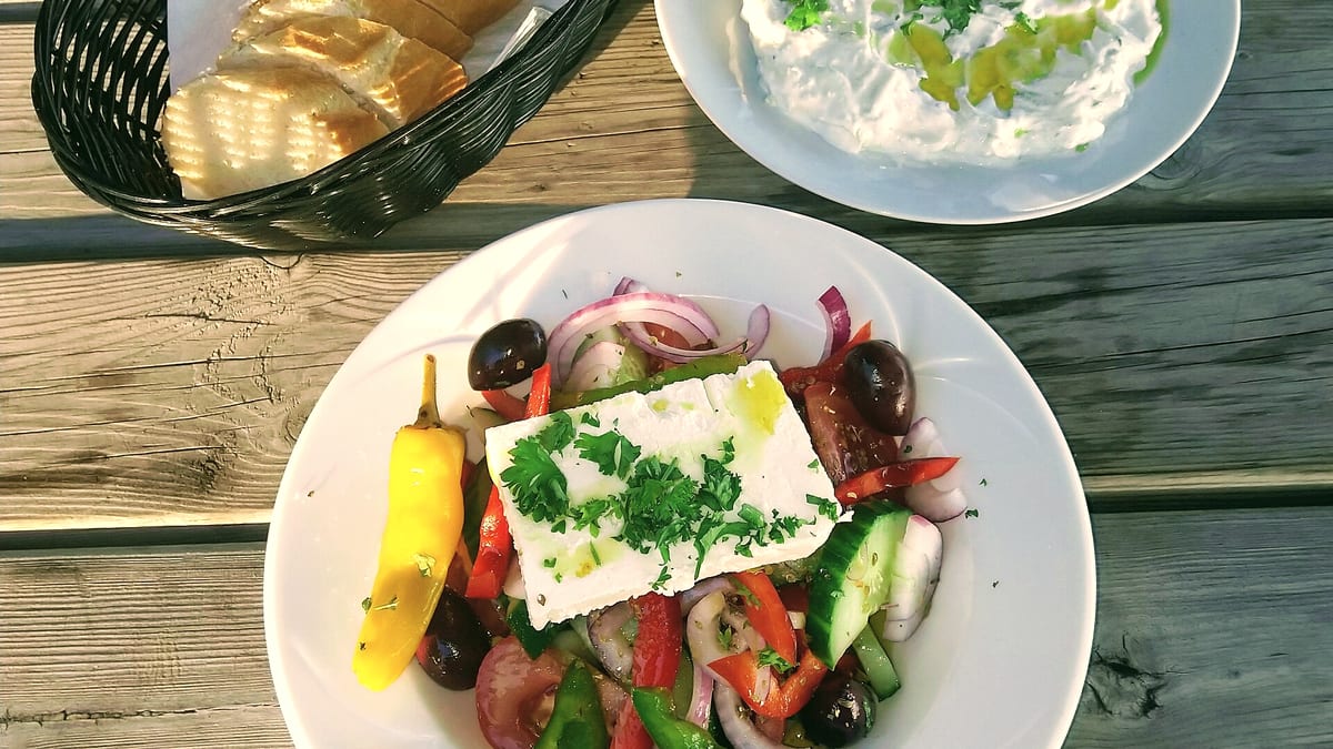 Weißkäse auf einem bunten Bauernsalat mit Oliven und Brot, sonnig auf einem Holztisch