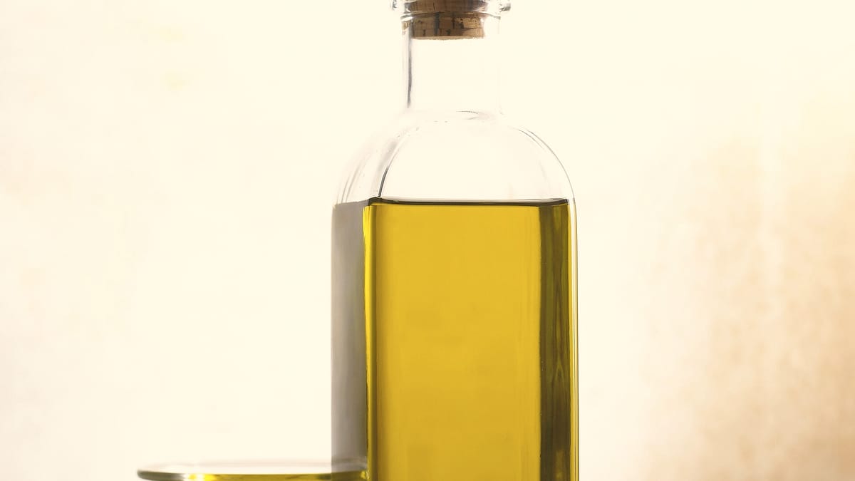 Flasche mit nativem albanischem Olivenöl extra neben einem gefüllten Glasschälchen