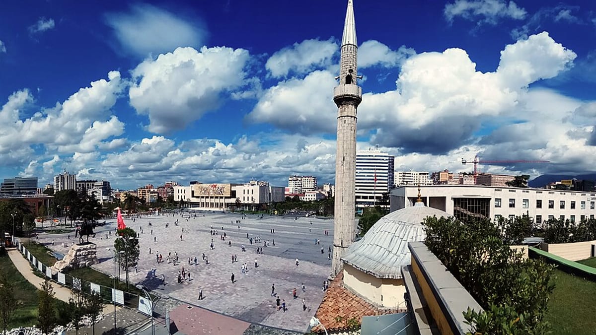 Sonniger Skanderbeg-Platz in Tirana mit Moschee, Minarett und Uhrturm unter blauem Himmel