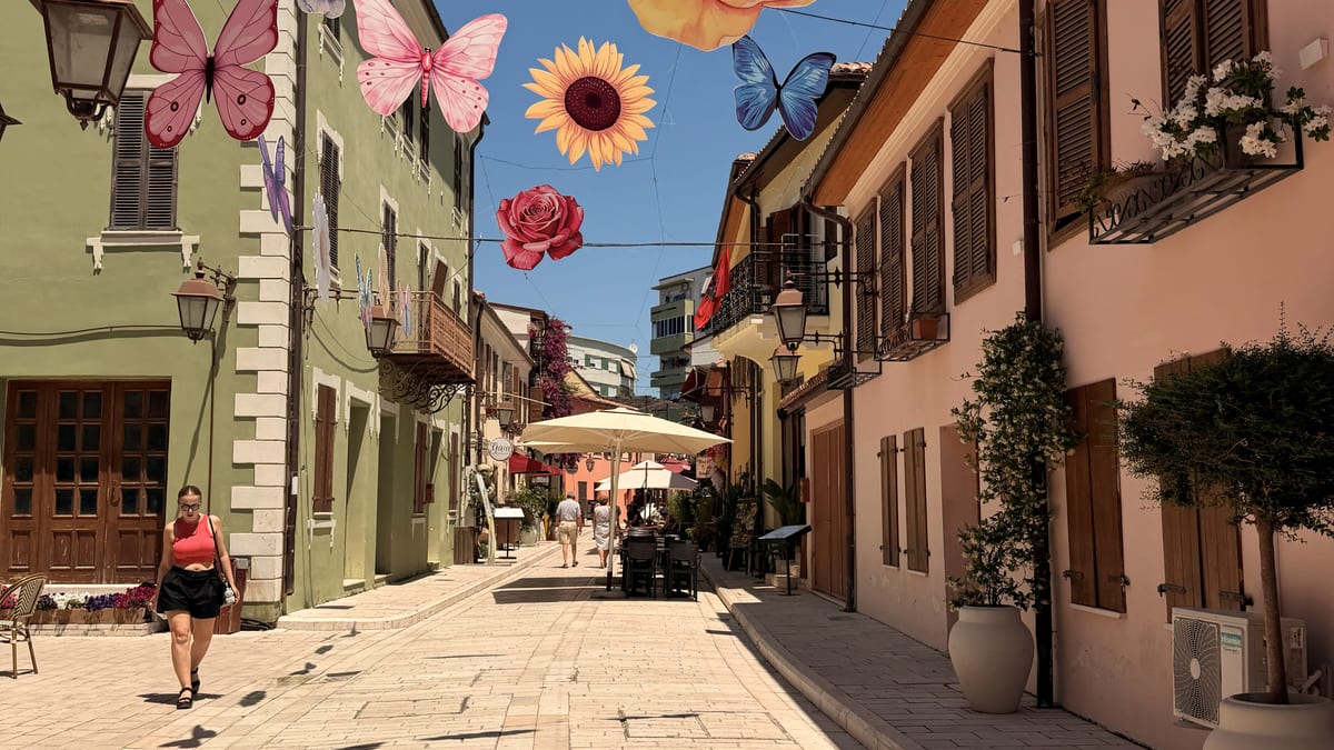 Sonnige Altstadtgasse in Vlora mit pastellfarbenen Häusern und Blumenschmuck